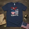 Navy blue t-shirt with "1776 2026 250 YEARS LIBERTY & INDEPENDENCE" text, eagle, and American flag shield graphic