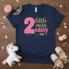 Navy blue t-shirt with "2 little miss sassy" text in pink and gold glitter. Features a large pink number "2"
