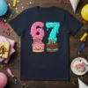 A navy t-shirt featuring the number 67 designed as dripping donuts and cakes, with sprinkles and candles, for a 67th