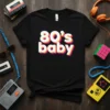 Black t-shirt with white, pink, and yellow layered text reading "80's baby", a retro 80s design