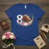 Blue t-shirt with a large number 8 and a brown horse with a flowing mane surrounded by pink and white