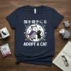 Adopt A Cat T-Shirt with Japanese text, showing a cartoon opossum in a cape holding a black cat