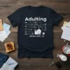 Adulting Please Wait snail graphic t-shirt with flowchart depicting chores and work, dark navy blue shirt