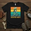 Adventure Awaits text with a cartoon frog riding a bicycle against a retro striped background on a black t-shirt