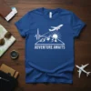 Blue t-shirt with white text "Adventure Awaits" over a graphic of mountains, sun, and an airplane, featuring a heartbeat line
