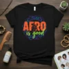 AFRO is good text with a raised fist graphic on a black t-shirt, featuring colorful Kente-inspired patterns and swirls