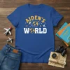 Blue t-shirt with "Aiden's World" text, featuring globes, rockets, and airplanes graphics for kids