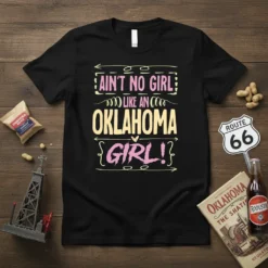 Ain't No Girl Like An Oklahoma Girl! text design on a black t-shirt, featuring yellow and pink lettering with decorative