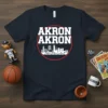 Navy blue t-shirt with "AKRON AKRON" in white bold letters above a white skyline graphic, all within a red circle