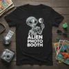Black t-shirt with a cartoon alien holding a vintage camera and flash, text reads "ALIEN PHOTO BOOTH"