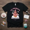 Black t-shirt featuring the quote "ALL YOU NEED IS CUPCAKES" above a whimsical cupcake tower graphic with clouds and stars