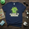 Allergic To Humans t-shirt design featuring a green alien wearing a mask and holding tissues, with a biohazard symbol