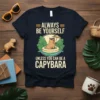 Always Be Yourself Unless You Can Be A Capybara quote on a navy t-shirt with a capybara relaxing in a
