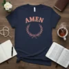 Navy t-shirt with the word "AMEN" in coral lettering above a coral laurel wreath and bow design