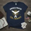 Navy t-shirt with "AMERICA PRAYED GOD ANSWERED" text, a white dove, praying hands, and golden sunburst graphic