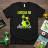 Armosaur Rex t-shirt design with a green cartoon dinosaur holding a trophy, wearing a sling, and standing on rocks