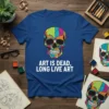 Geometric skull graphic with "Art Is Dead, Long Live Art" text on a blue t-shirt, art supplies in background