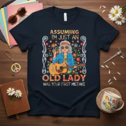 T-shirt design with text "Assuming I'm Just An Old Lady Was Your First Mistake", featuring a hippie woman playing guitar