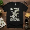 Back in My Day We Scrolled Newspapers quote on a black t-shirt, featuring a graphic of an older man reading