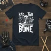 Bad Two The Bone graphic tee with a skeleton playing a guitar, bold white typography, and punk rock style