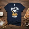 Navy t-shirt with "BAKER BAKER" text, a chef's hat, rolling pin, whisk, and croissants graphic