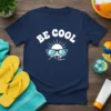 BE COOL text with sunglasses, sun, and wave graphic on a navy blue t-shirt