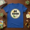 Blue t-shirt with black BE GOOD text, a smiling sun, green leaf, and heart graphic inside a yellow circle