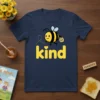 Cute bee graphic with "kind" text and honey pot on a navy blue t-shirt, representing the Be Kind message