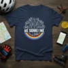 Be Someone t-shirt with white text, city skyline, bicycles, scooter, and rainbow graphic