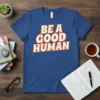 BE A GOOD HUMAN text design on a blue t-shirt, bold cream lettering with orange outline