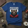 РОССИЯ text above a fierce brown bear's head against the Russian flag and pine forest background on a blue t-shirt