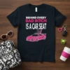 Black t-shirt with white and pink text "BEHIND EVERY BAD BITCH IS A CAR SEAT" and a pink sports car