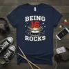 Being 16 Rocks text with drum graphic, music notes, and stars on a navy blue t-shirt