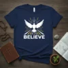 Navy blue t-shirt with white text "BELIEVE" and a white dove with outstretched wings, surrounded by yellow and white rays