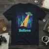 Believe t-shirt design with a UFO abducting a person in a city, featuring the word "Believe" below