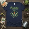 Bentnley Gardens t-shirt featuring a green floral wreath with a potted plant, gate, and gardening tools graphic