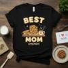 Best Mom Omomom. text with stacked cookies, rolling pin, and coffee cup graphic on a black t-shirt