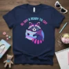 Bi, Shy & Ready To Cry text with a cute, sad raccoon holding a pillow graphic on a navy t-shirt