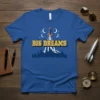 Blue t-shirt with "BIG DREAMS" text, a rocket ship launching over a city skyline, and crescent moons with stars