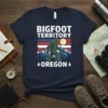 Bigfoot Territory Oregon t-shirt with a walking Bigfoot graphic, mountains, and retro stripes. Features the text "BIGFOOT TERRITORY OREGON"