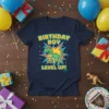 Birthday Boy Level Up dinosaur t-shirt with a T-Rex wearing a party hat and gaming controller graphic