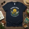 Bloom & Grow Embrace the Wildflower Spirit text with a central sunflower and daisy graphic on a navy t-shirt