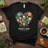 Black t-shirt with a heart-shaped floral design and the text "BLOOM & GROW Inspired by Nature"