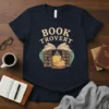 Book Trovert quote on a navy t-shirt with a graphic of an open book, bookshelves, and a yellow armchair