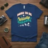Retro "Born to Be Wildly Awesome" text design with mountains, trees, and stars graphic on a navy t-shirt