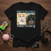 Black t-shirt with "Born to Dilly Dally Forced to Lock In" text and contrasting cat images, one knitting, one in