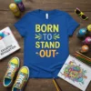 Born to Stand Out text design on a royal blue t-shirt, featuring vibrant yellow, green, and orange lettering with decorative