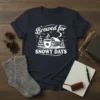 Brewed for SNOWY DAYS text with a steaming coffee cup, cabin, and pine trees graphic on a navy t-shirt