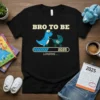 Bro To Be Loading 2025 T-Shirt featuring a cute dinosaur pushing a baby stroller with loading bar graphic