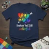 Broken Yet Still Colorful T-Shirt featuring a rainbow broken heart with an arrow, white text above colorful text below